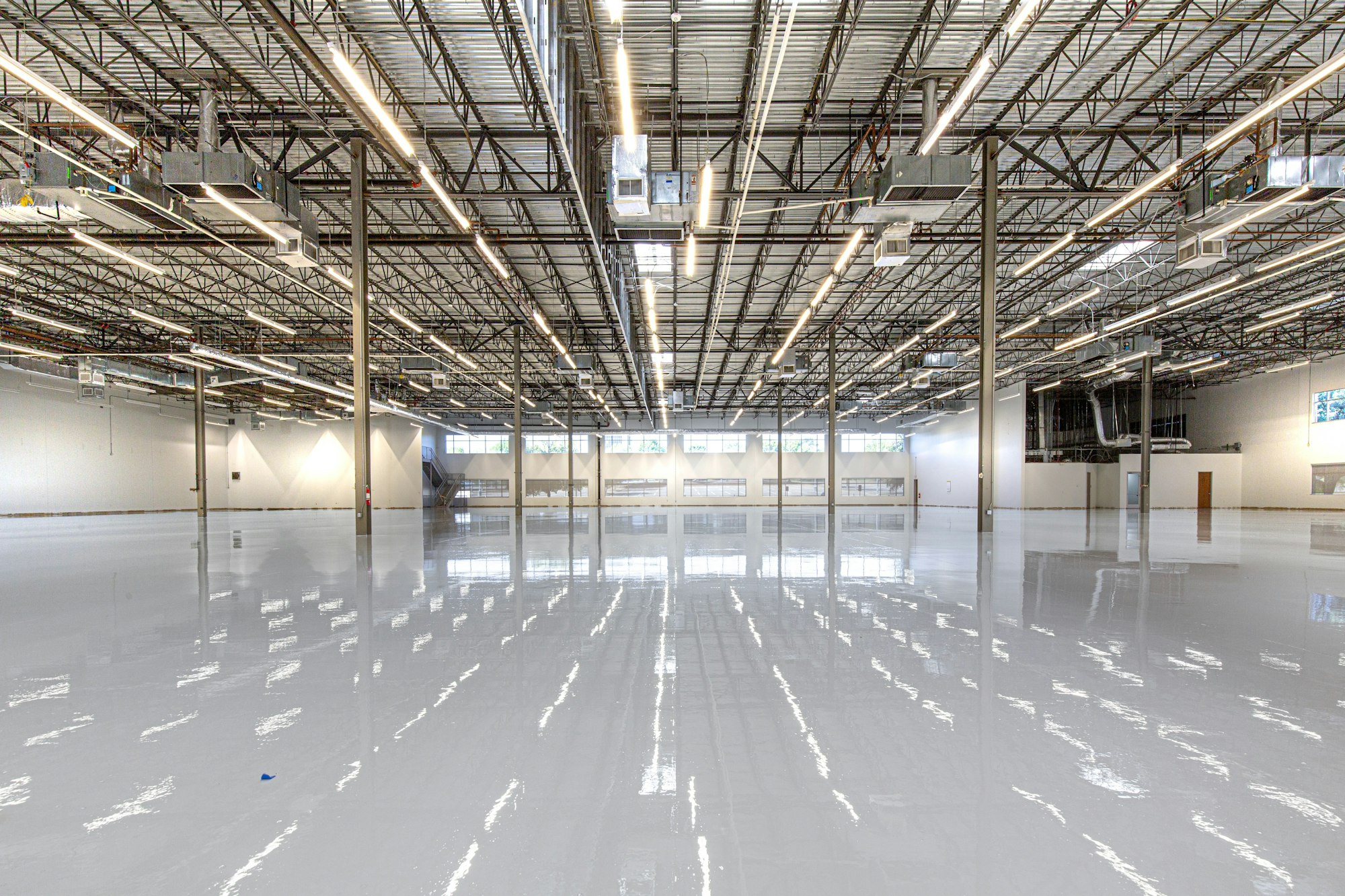 A vast industrial warehouse with a mirror-finish polyaspartic floor coating reflecting the overhead lighting.
